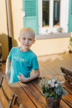 boy with flowers at the table. the boy stands near a wooden table. On the table is a vase of flowers. Youth and decay.