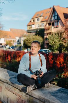 Man Sitting on Stairs in Old European City And Holding Photo Camera. Contemporary Stylish Blogger And Photographer