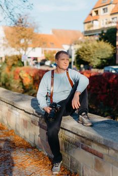 Man Sitting on Stairs in Old European City And Holding Photo Camera. Contemporary Stylish Blogger And Photographer