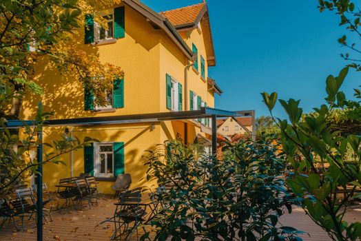 Image of a empty coffee tables arranged in backyard of a house. Autumn in Germany, Europe. Outdoor table in street cafe. autumn outdoor cafe wooden furniture old europe. Autumn photo of old-fashioned cozy and empty outdoor cafe with wooden furniture in a European town. Cafe concept