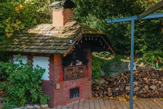 An Old Stove And Firewood For It In The Yard In The Village. Old Stone Fireplace Outdoors In The Fall. Traditional Brick Oven With Wood For Baking Bread Outdoor In Europe.