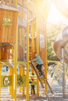 boy playing on the children's playground, a boy on a playground in the park climbs up a climbing wall. Kids having fun and sliding on outdoor playground. Kids Enjoying. A child climbs up an alpine grid in a park on a playground on a hot summer day. children's playground in a public park, entertainment and recreation for children, mountaineering training.