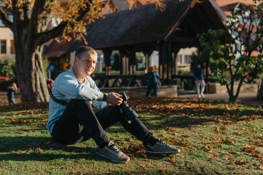 Professional photographer taking picture of beautiful autumn park. man professional photographer sit with camera in autumn park