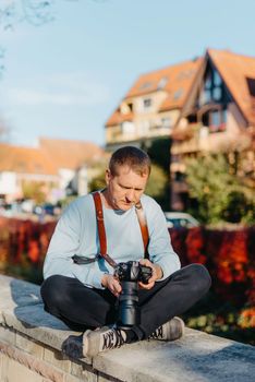 Man Sitting on Stairs in Old European City And Holding Photo Camera. Contemporary Stylish Blogger And Photographer