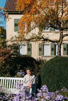 a girl sits on a bench in the park and enjoys the sun. Portrait young adult attractive woman enjoy sitting on bench and relaxing calm carefree rest in city park against green grass and trees on sunny day. Single female person relaxing chilling outdoors