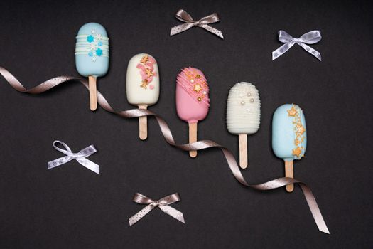 Cake pops ice creams with ribbon and bows on black background. Top view.