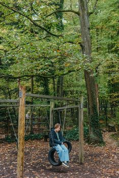 A teenage girl sitting on a swing on the park. Pensive sad child. Thoughtful Sad Teenager Girl Sitting On Playground Roundabout. teenage girl sad on the swing in the park