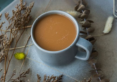 Hot orange milk tea in a blue ceramic cup, Sweet refreshment thai milk tea on ceramic and dried flowers on ceramic plate. Selective focus.