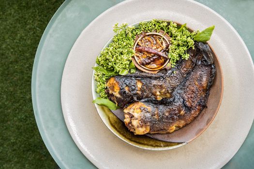 Grilled catfish (Roasted Catfish) and neem leaf served with sweet tamarind fish sauce (Sadao Nam Pla Wan) in plate. The Signature of Thai traditional local food, Top view, Selective focus.