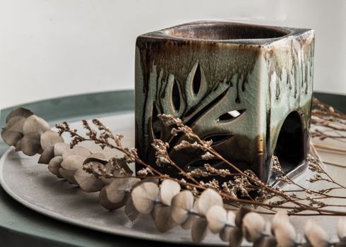 Candle aroma oil lamp and dried flowers on ceramic plate. Handmade ovens for ceramic aromatic essences, Relaxation and meditation concept, No focus, specifically.