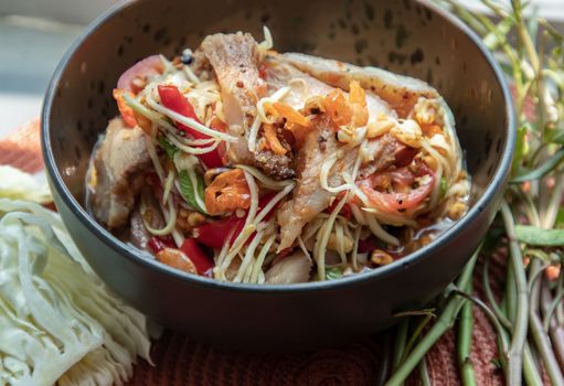 Close-up of Thai papaya spicy salad (som tum) mix grilled pork neck on ceramic dishes. delicious spicy Thai food, Selective focus.