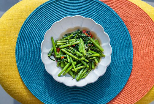 Stir-Fried Chinese Morning Glory or Water Spinach (pak boong fai daeng) seasoned with chili and soy sauce on white plate. Asian food style, Selective focus.