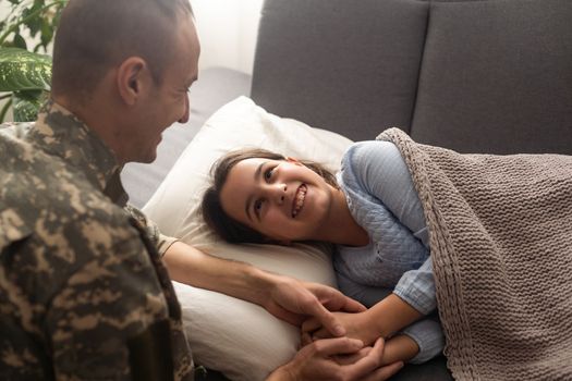 Soldier kissing his daughter while she sleeping on a bed at home