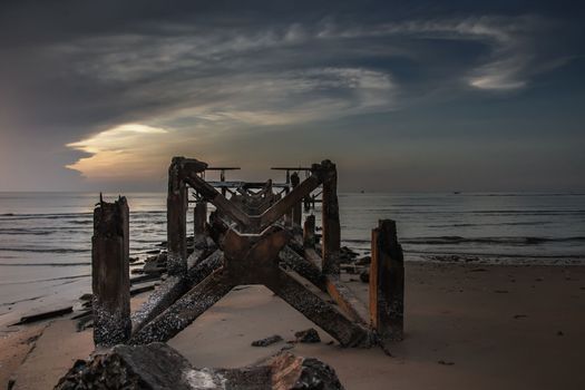 Looking out at Broken old structure remains of pier in the sea. Small wave crashing into the textured rusty pier posts in the during beautiful twilight in the sea. No focus, specifically.