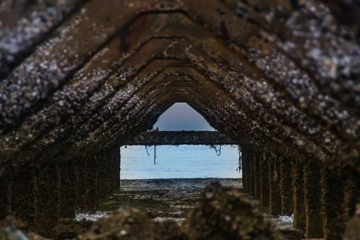 View under at Broken old structure remains of pier in the sea. Small wave crashing into the textured rusty pier posts in the during beautiful twilight in the sea. No focus, specifically.