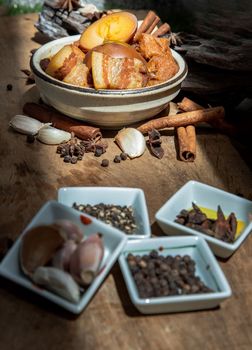 Boiled egg (kai pa lo) and Belly Pork Chinese Five-Spice Stewed with Tofu in brown sauce decorated with anise star, cinnamon, garlic and black pepper on old wooden table, Asia food, Selective focus.