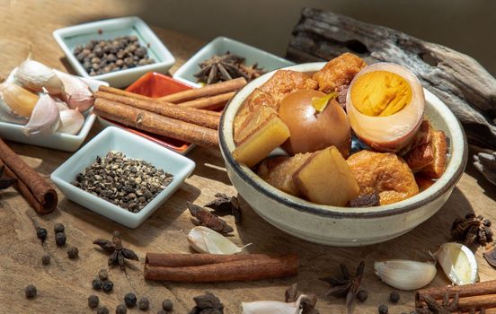 Boiled egg (kai pa lo) and Belly Pork Chinese Five-Spice Stewed with Tofu in brown sauce decorated with anise star, cinnamon, garlic and black pepper on old wooden table, Asia food, Selective focus.