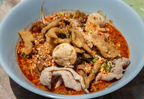 Egg noodles in Thai spicy soup with braised pork, pork balls and fatty pork rinds in white bowl. Thai food, Selective focus.