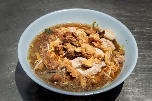 Instant noodles in braised pork soup with pork balls and fatty pork rinds in white bowl. Thai food, Selective focus.