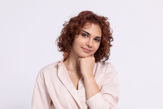 A gentle smile on her face. A European woman with chestnut-colored hair. A girl with fair skin and curly short hair looks straight ahead.