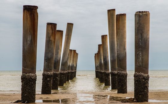 The leaning pillars of the old Pier looking toward beach on a sunny day. Selective focus.