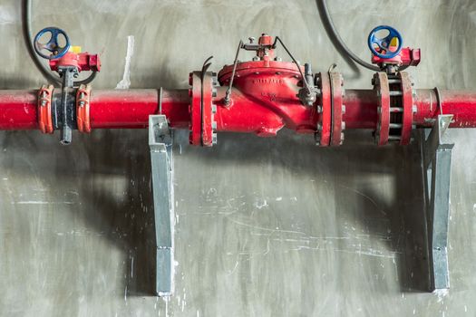 Red water or gas pipeline with gate pressure valve on concrete wall. Industrial tubes and valves, Line pipe industrial and extinguisher pump, Copy space, Selective focus.