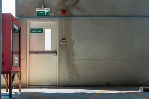 Fire exit door or Fire escape door with exit sign and Red fire fighting equipment cabinet in a car parking building. Safety first concept. Copy space, Selective focus.