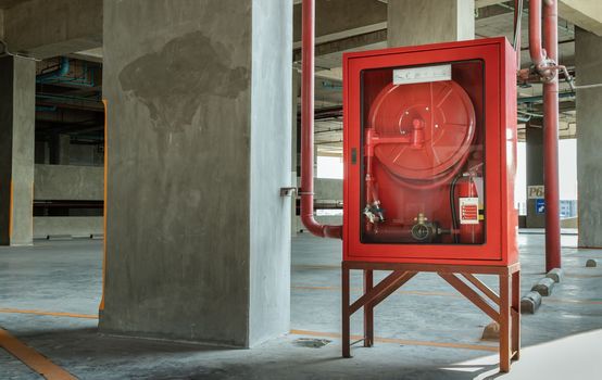 A red fire fighting equipment cabinet or fire extinguishing cabinet of fire protection set is located in car parking. Emergency Fire Extinguisher, Rolled Pipe, Hydrant and water hoses, Safety first concept. Selective focus.