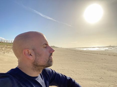 Backlight profile of a man breathing deep fresh air alone in idyllic empty beach.