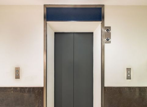 Elevator chrome metal with closed door in condominium. Lift transportation floor to floors with push switch for up and down. Selective focus.