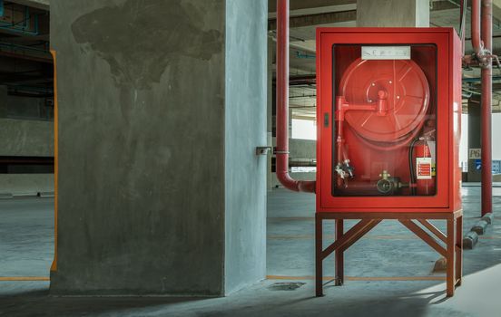 A red fire fighting equipment cabinet or fire extinguishing cabinet of fire protection set is located in car parking. Emergency Fire Extinguisher, Rolled Pipe, Hydrant and water hoses, Safety first concept. Selective focus.
