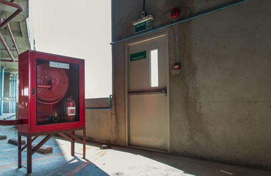 Fire exit door or Fire escape door with exit sign and Red fire fighting equipment cabinet in a car parking building. Safety first concept. Selective focus.