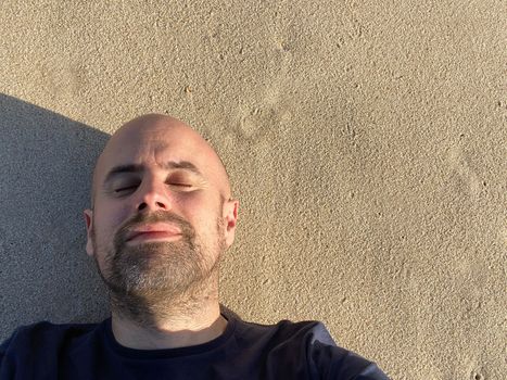 Headshot of happy man with closed eyes meditating laying on the sand healing stress on the beach with copy space.