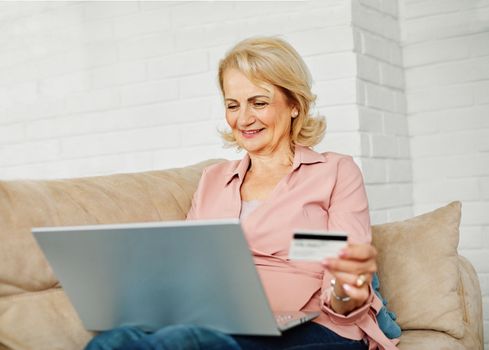 portrait of happy smiling senior couple using laptop and credit card at home