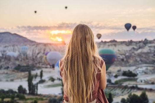 Tourist woman looking at hot air balloons in Cappadocia, Turkey. Happy Travel in Turkey concept. Woman on a mountain top enjoying wonderful view.
