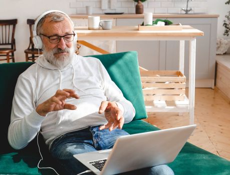 Elderly man making video call on laptop in room waving to screen and chatting with children - modern technologies communication internet