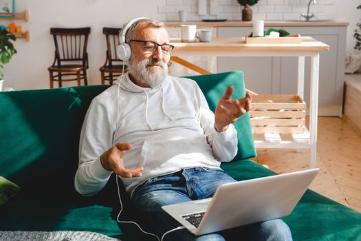 Elderly man making video call on laptop in room waving to screen and chatting with children - modern technologies communication internet