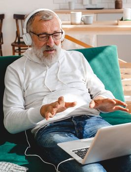 Elderly man making video call on laptop in room waving to screen and chatting with children - modern technologies communication internet