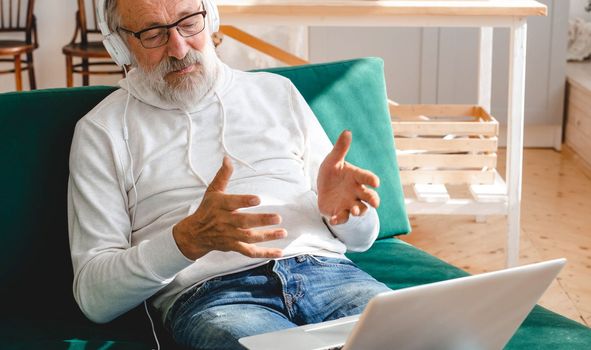 Elderly man making video call on laptop in room waving to screen and chatting with children - modern technologies communication internet