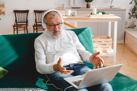 Elderly man making video call on laptop in room waving to screen and chatting with children - modern technologies communication internet