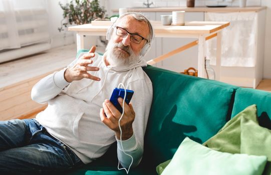 Elderly man making video call on laptop in room waving to screen and chatting with children - modern technologies communication internet