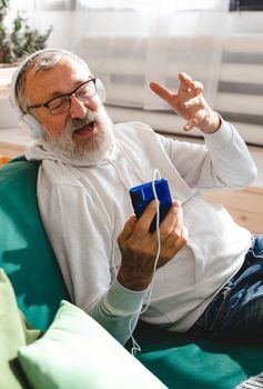 Elderly man making video call on laptop in room waving to screen and chatting with children - modern technologies communication internet