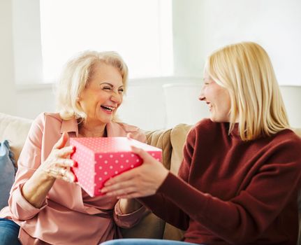 Daughter or granddaughter surprises her mother or grandmother with present on mother's day or birthday at home