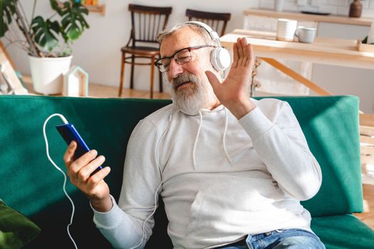 Elderly man making video call on laptop in room waving to screen and chatting with children - modern technologies communication internet