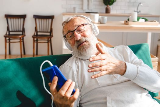 Elderly man making video call on laptop in room waving to screen and chatting with children - modern technologies communication internet