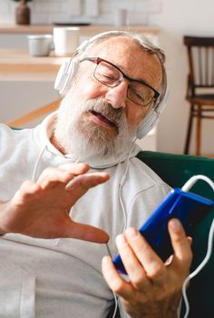 Elderly man cool bearded old man using mobile phone for video call - happiness elderly lifestyle people concept. Video call on smartphone in room waving to screen and chatting with children - modern technologies communication and internet.