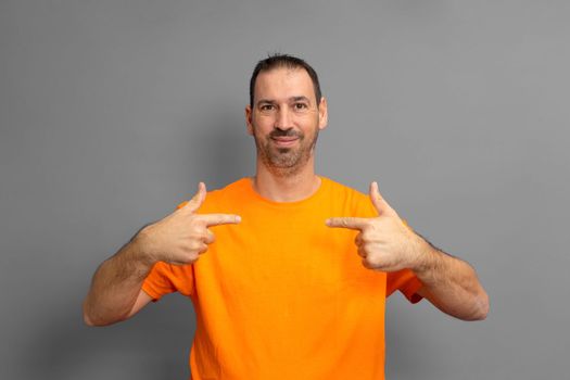 Portrait of handsome Hispanic bearded man pointing to himself puzzled at being chosen. Amazed attractive european man over gray background, he has a confused expression. Surprise concept