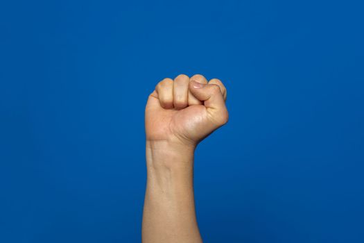 Man's fist seized with power isolated on blue background. Symbol of rebellion and uprising of the working classes oppressed by the elites