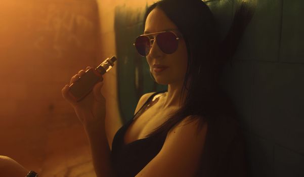 Fashion art portrait of beauty model woman in bright lights with colorful smoke. Smoking girl, Close up of a female inhaling from an electronic cigarette. High quality photo