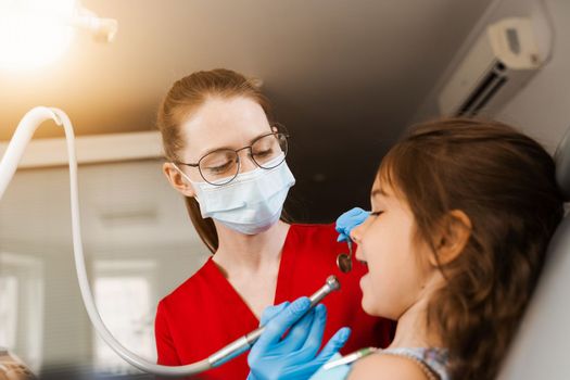 Child dentist with dental drill treats child girl in dentistry clinic. Dental filling for child patient